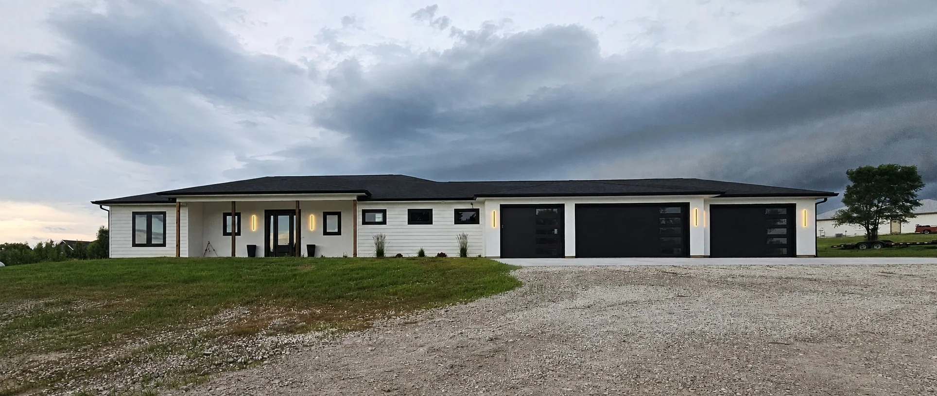 Completed Midwest Custom Homes residence at dusk, a white single-story home with black garage doors under an open Midwest sky