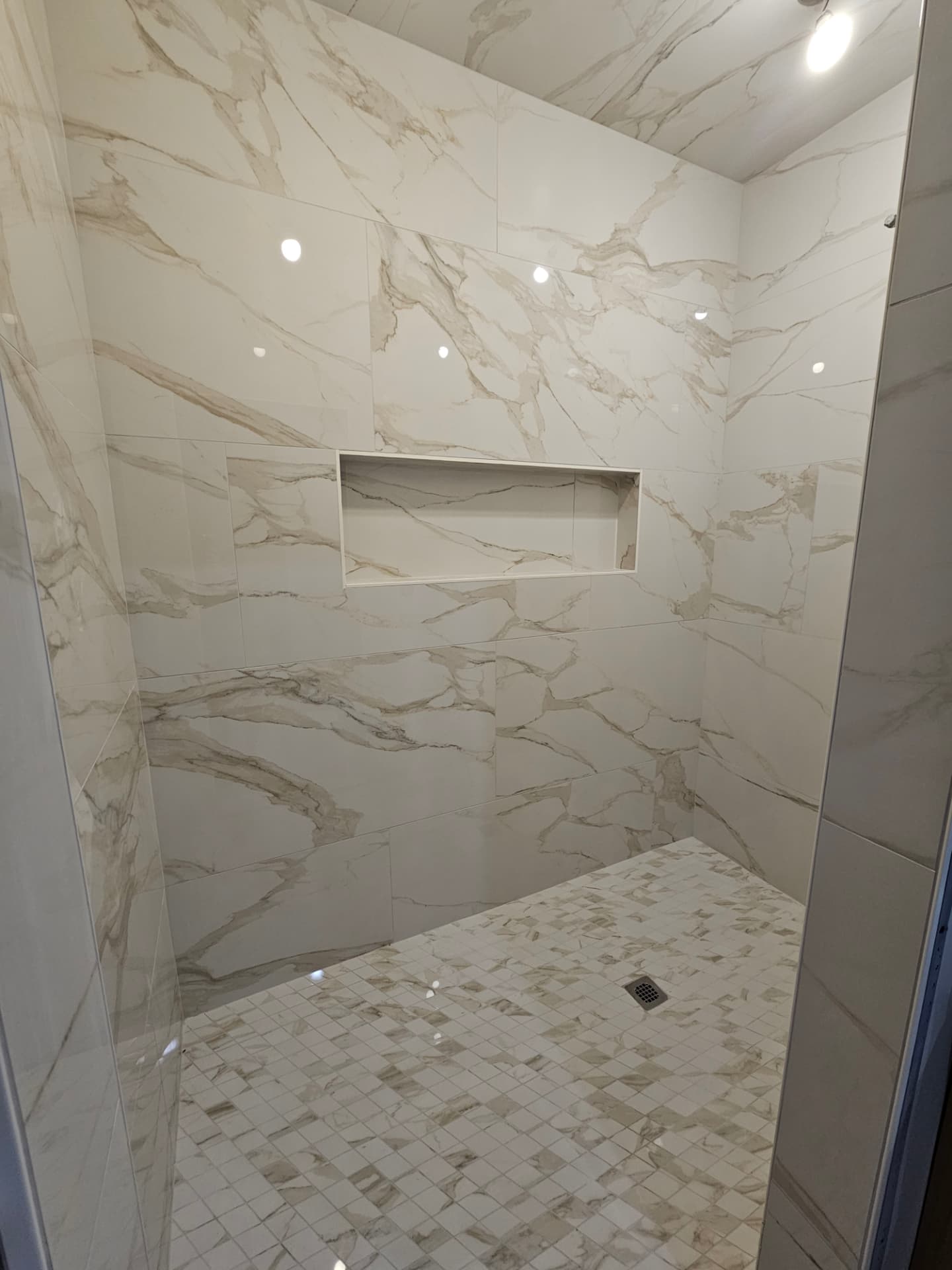 Custom walk-in shower with large-format marble-look tile, mosaic floor and built-in wall niche.